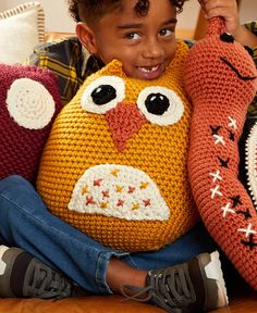 a young boy sitting on a couch holding two knitted owl pillows in front of his face