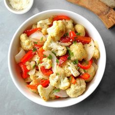 a white bowl filled with cauliflower and red peppers next to a cutting board