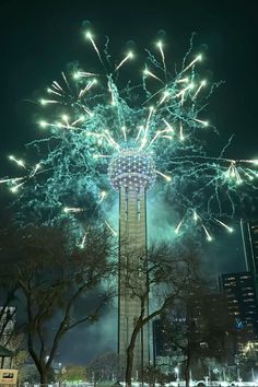 fireworks are lit up in the night sky above a tall tower with trees and buildings