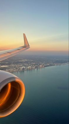 an airplane wing flying over the ocean at sunset