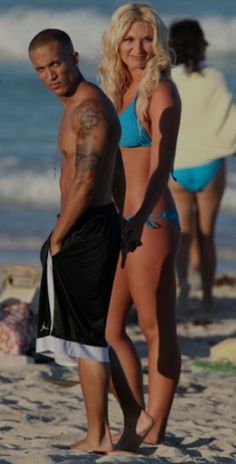 a man and woman standing on top of a sandy beach next to the ocean in bikinis