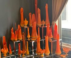 an assortment of orange vases on display in front of a window