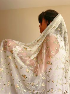 a woman wearing a white veil with flowers on it is standing in front of a wall