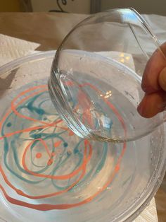 someone is pouring water into a bowl with orange and blue swirls on the bottom