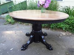 a wooden table sitting on top of a cement ground next to some bushes and flowers