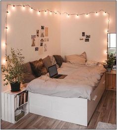 a laptop is sitting on top of a bed with lights strung over the headboard