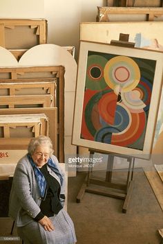 an older woman sitting in front of paintings