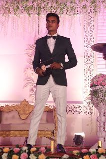 a man in a tuxedo is standing on the stage with flowers around him