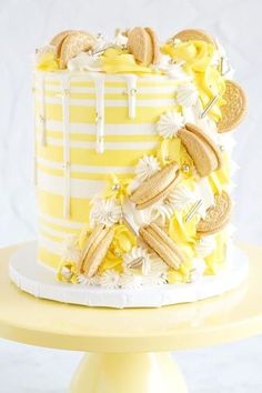 a yellow and white striped cake with cookies on the top is sitting on a pedestal