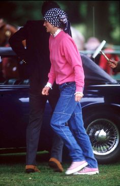 an old man walking in front of a car with another person standing next to him