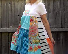 a woman standing in front of a wooden fence wearing a dress with colorful patches on it