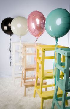 three balloons are tied to the back of two wooden chairs, and one balloon is on top of another chair