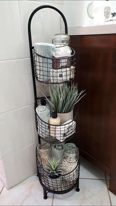 three tiered metal basket with plants and towels on the floor next to a sink