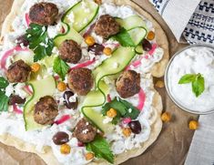 a pizza topped with meatballs and cucumbers next to a bowl of yogurt