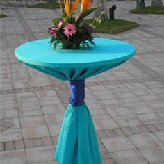 a blue table with flowers on it sitting in the middle of a brick walk way