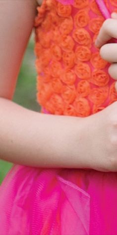 a close up of a person's hand holding an orange and pink flowered dress