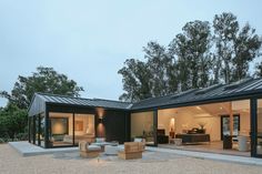 a modern house with glass walls and lots of furniture in the back yard at dusk