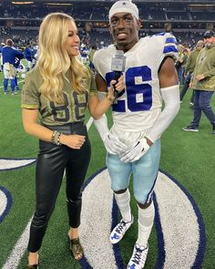 a woman standing next to a football player on top of a field with a microphone