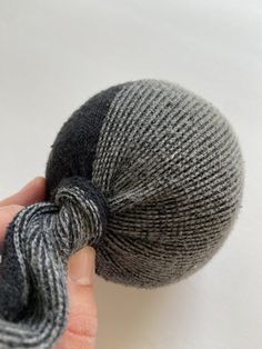 a hand holding a gray and white knitted ball with a knot at the end