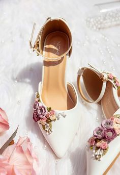 two pairs of shoes with flowers on them sitting on a white furnishing next to pink roses