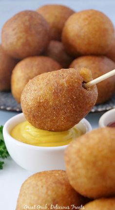 Deep fried sausage bites with a small bowl of mustard on a plate with one being held up by a toothpick.