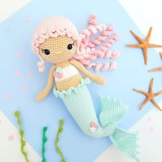 a crocheted mermaid doll sitting on top of a blue surface next to starfish