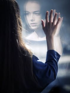 a woman is holding her hands up to the light coming from behind her, and she is looking at herself in the mirror