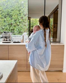 a woman holding a baby in her arms while standing next to a kitchen counter top