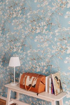 a purse sitting on top of a table next to a lamp and book shelf in front of a floral wallpaper