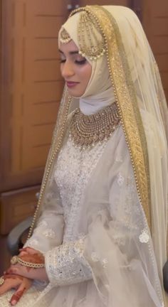 a woman in a white dress and veil sitting on a chair with her hands clasped