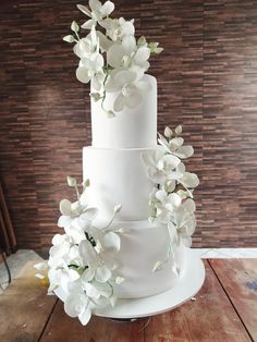 a three tiered white wedding cake with flowers on the top and bottom, sitting on a wooden table