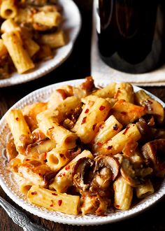 pasta with mushrooms and sauce on a white plate next to a glass of black wine