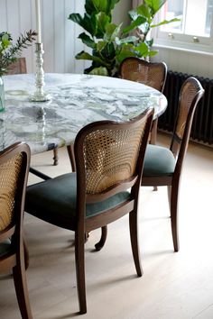 a marble table with chairs around it in front of a window and potted plant