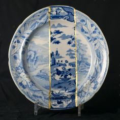 a blue and white plate sitting on top of a wooden stand in front of a black background