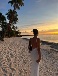 a woman standing on top of a sandy beach next to the ocean with palm trees