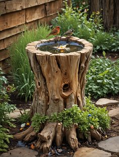 a bird bath sitting on top of a tree stump next to a flower garden filled with plants