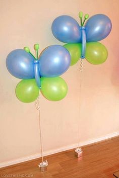 two blue and green balloons in the shape of butterflies on wooden floor next to wall