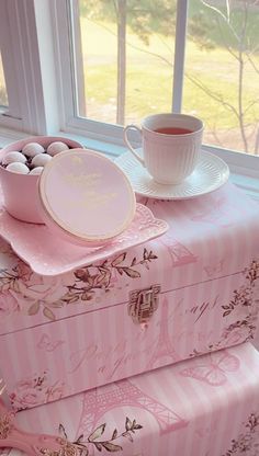 two pink boxes with plates and cups sit on a window sill next to a cup