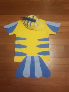 a yellow and blue fish shirt laying on top of a wooden floor next to a pair of scissors