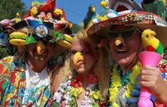 three people dressed in colorful clothing and hats with birds on their heads, one holding a pink object