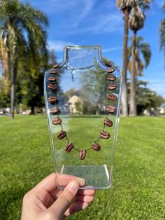 a person holding up a necklace in front of some palm trees and green grass on a sunny day