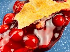 a piece of pie sitting on top of a blue plate covered in red jelly and cherries