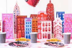 a table topped with cups and plates covered in paper cut outs next to a cityscape