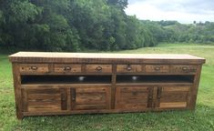 a large wooden dresser sitting on top of a lush green field with trees in the background