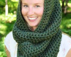 a woman wearing a green knitted cowl scarf in the woods smiling at the camera