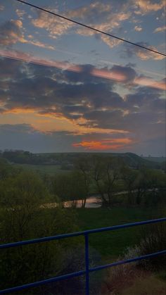 the sun is setting over an open field with trees and water in the foreground