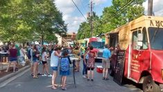 many people are standing in the street near food trucks