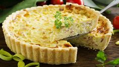 a quiche is cut into pieces and placed on a wooden table with fresh vegetables