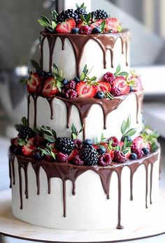 a three tiered cake with berries and chocolate drizzled on it's sides