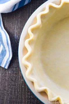 an uncooked pie crust sits on a plate next to a blue and white napkin